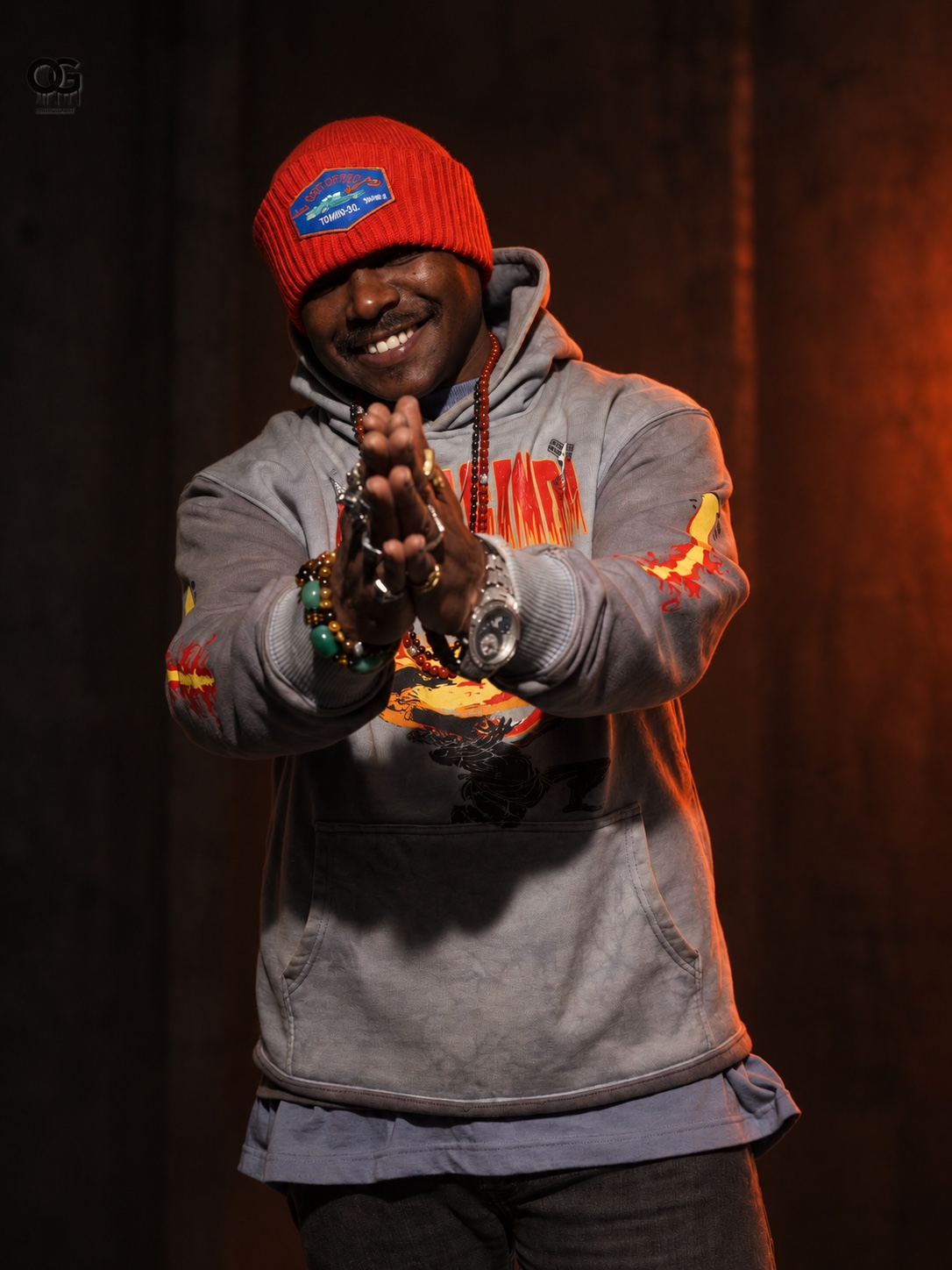 Chaycin Change standing with clasped hands, wearing a red beanie
